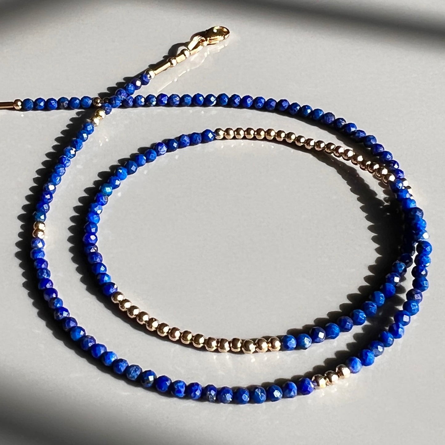 Elegant faceted lapis lazuli and 14K gold bead strand necklace, featuring rich blue gemstones and luxurious gold accents for a timeless look