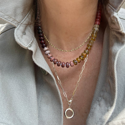 A necklace featuring a luminous baroque pearl pendant and sterling silver clasp, accented with vibrant gemstone beads in rich, earthy tones.