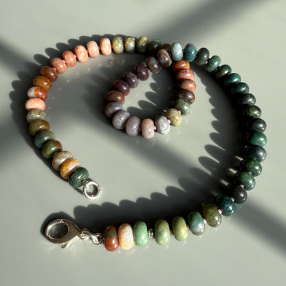 A handcrafted necklace featuring polished multicolored gemstone beads arranged in a gradient pattern, with a silver clasp.