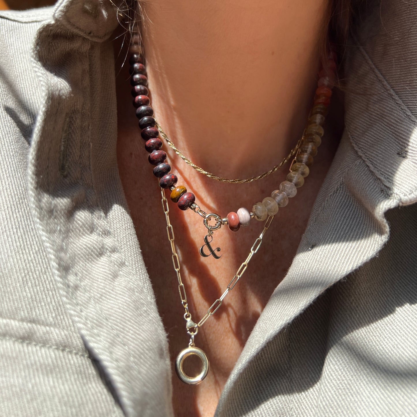 Close-up of a layered necklace look, featuring a center necklace with a lustrous baroque pearl pendant and sterling silver clasp, styled with complementary gold chain necklaces.