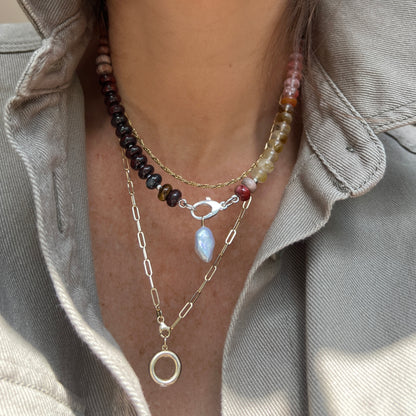 A close-up of a layered necklace set, highlighting the center necklace with a baroque pearl pendant and sterling silver clasp, styled for an elegant and modern look.