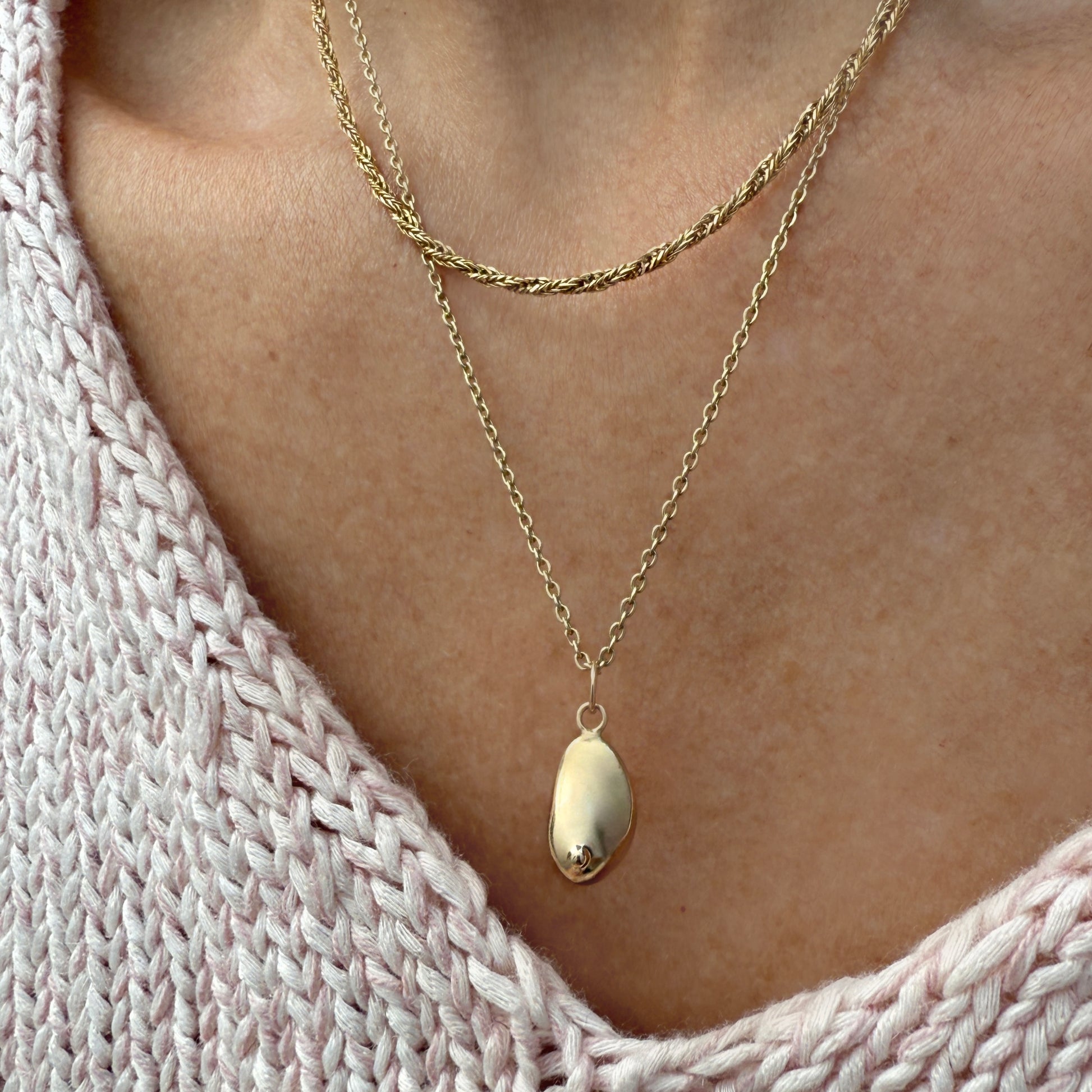 Gold breast charm necklace catching sunlight on a warm brown surface