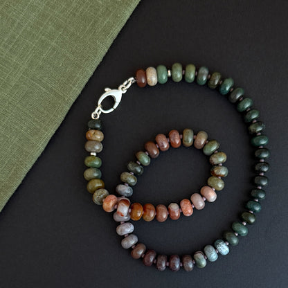A gemstone necklace in a circular layout, featuring rich tones and textures with a silver lobster clasp at the end.