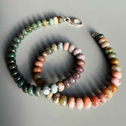 A colorful gemstone necklace with smooth, rounded beads in earthy shades of green, brown, and pink, elegantly arranged and secured with a silver clasp.