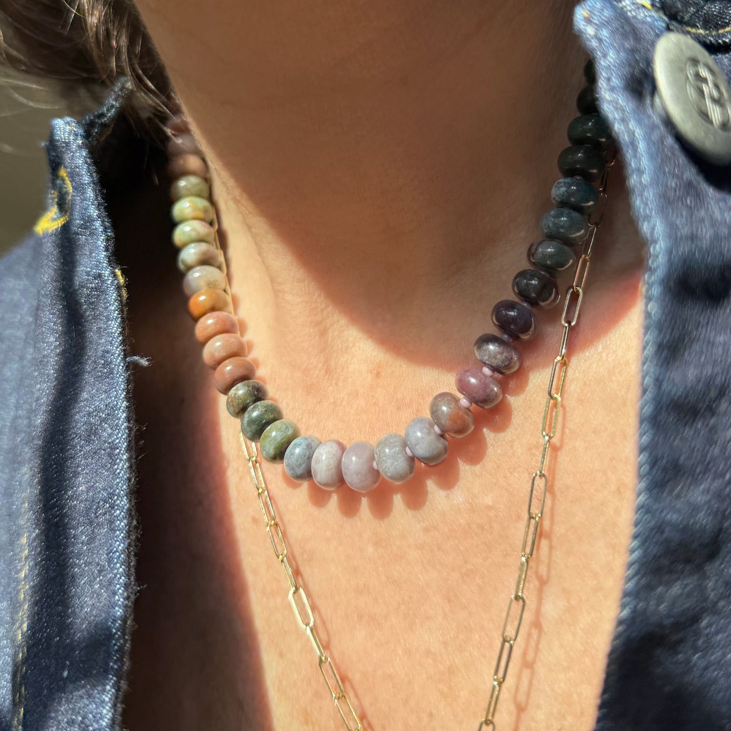 A vibrant beaded necklace showcasing earthy tones of green, orange, pink, and purple, highlighted by sunlight and shadows.