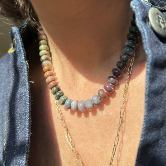 A vibrant beaded necklace showcasing earthy tones of green, orange, pink, and purple, highlighted by sunlight and shadows.