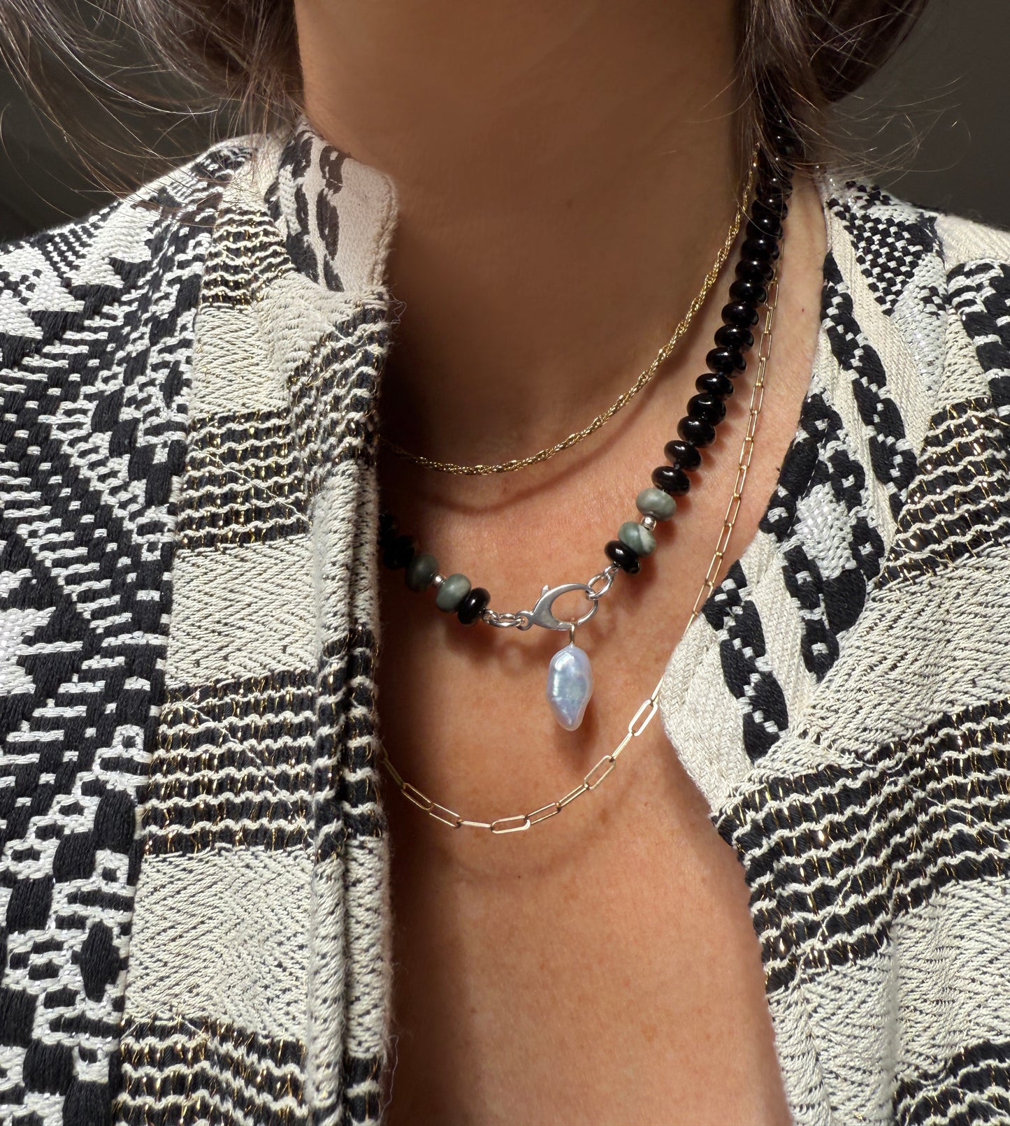 A necklace with black beads and a few gray or greenish beads near a silver clasp, featuring a dangling blue crystal or gemstone in the center.