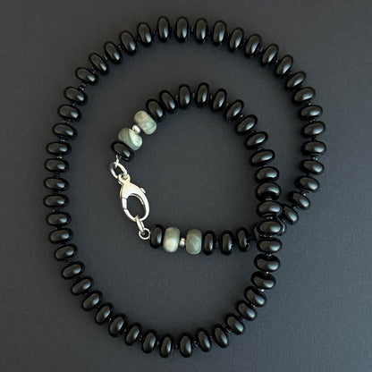 A beaded necklace with black beads and a few lighter gray or greenish beads near a silver clasp.