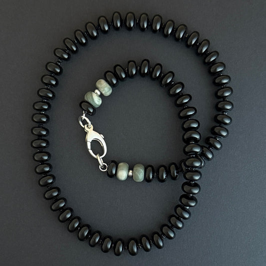 A beaded necklace with black beads and a few lighter gray or greenish beads near a silver clasp.