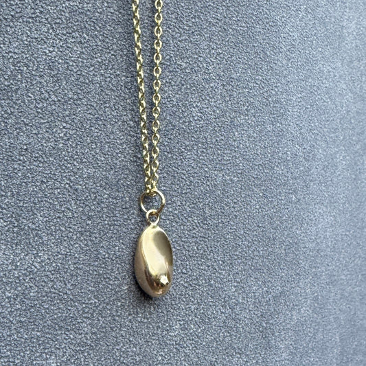 Artistic gold pendant shaped like a breast, hanging from a fine chain