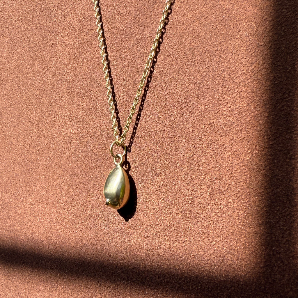 Close-up of gold breast pendant necklace casting a shadow on metallic backdrop
