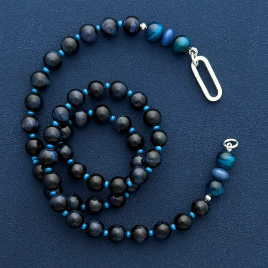 Dark blue lapis and matte black beads with a silver push clasp, coiled flat lay on blue, by SOLO Jewelry